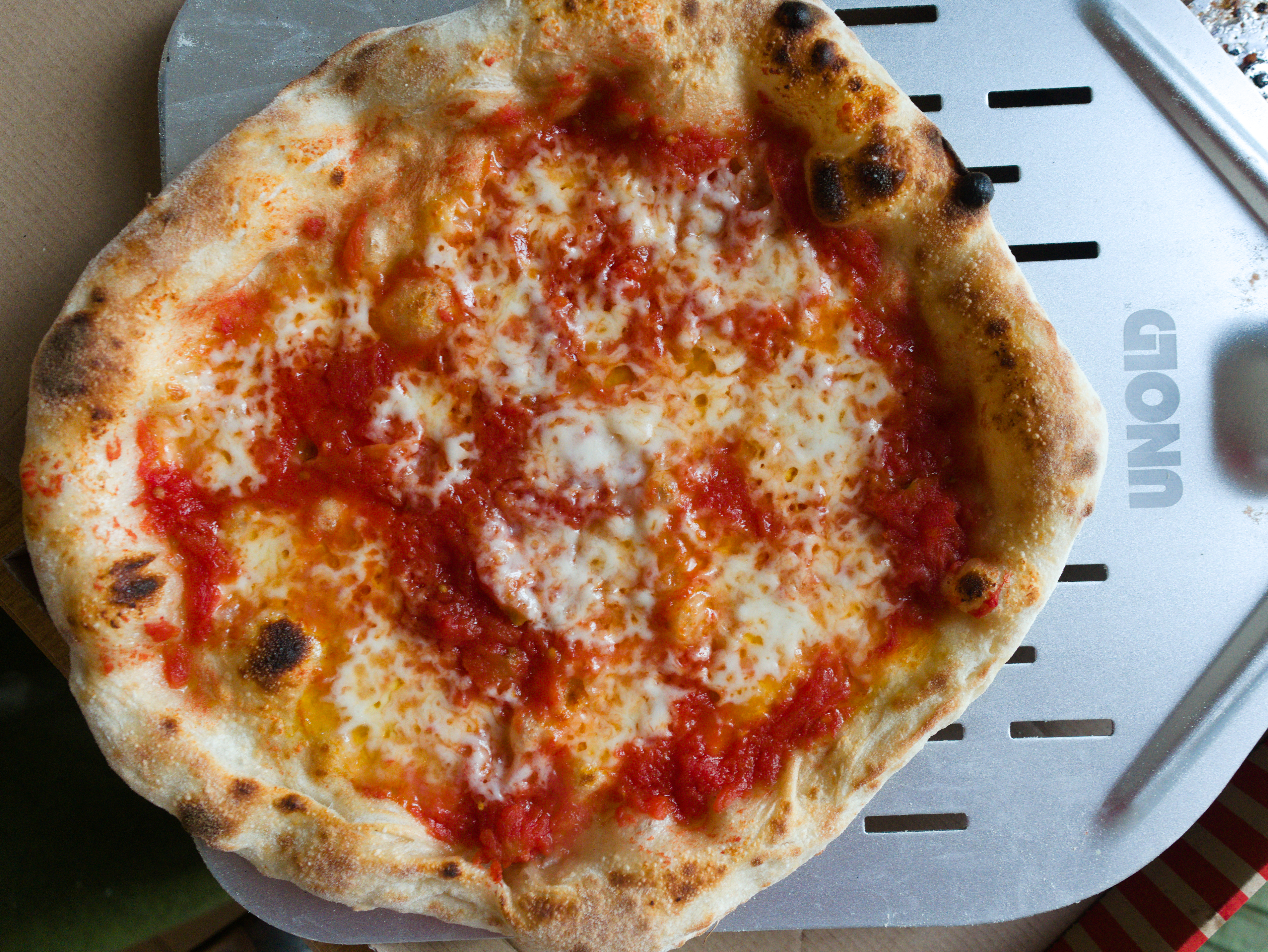 Eine fertig gebackene Pizza ist auf einem Pizzaschieber und kommt frisch aus dem Ofen.