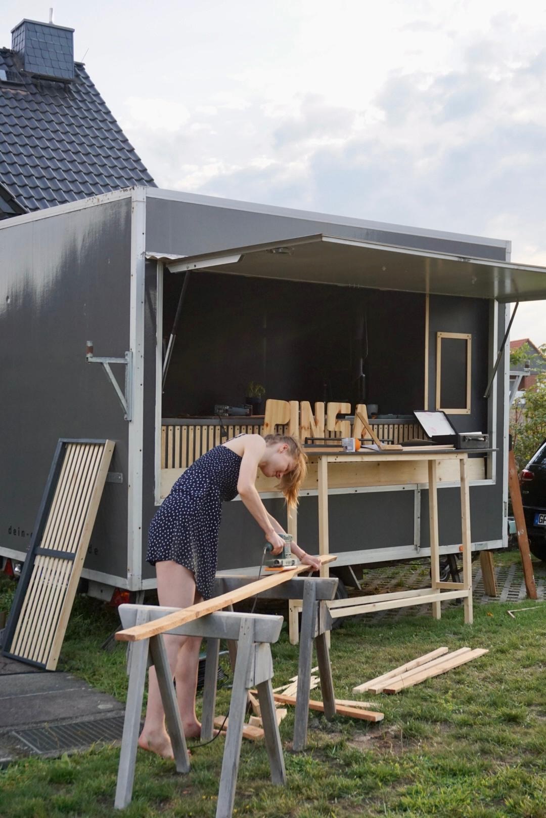 Sägen vor dem Foodtruck und Holzlatten schleifen für den Pizzaverkaufsanhänger